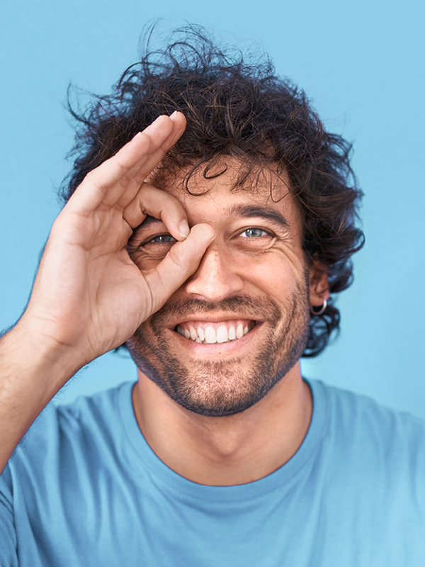 Ein Mann formt mit seinen Fingern einen Kreis und hält ihn lächelnd vor sein Auge, blickt hindurch.